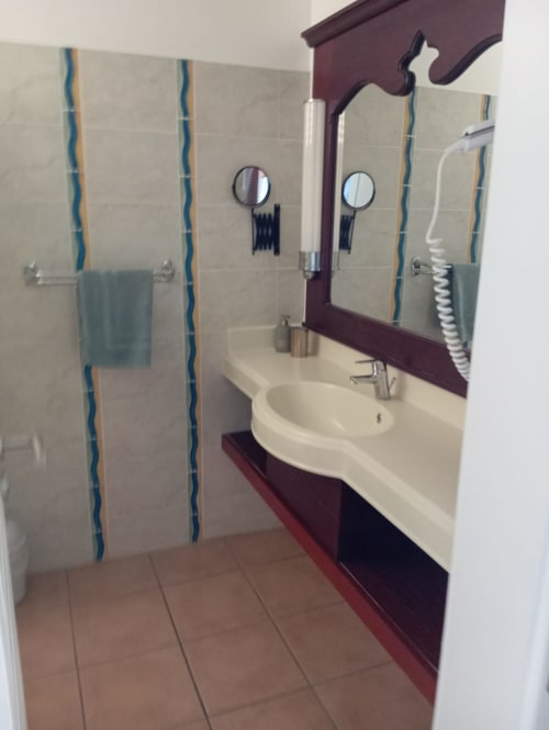 Salle de bain moderne aux Tropic Apartments avec vasque courbe, meuble burgundy, carrelage rayé et miroir à Sainte-Anne