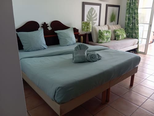 Chambre studio lumineuse avec literie turquoise, mobilier en bois et balcon vue mer aux Tropic Apartments, Sainte-Anne