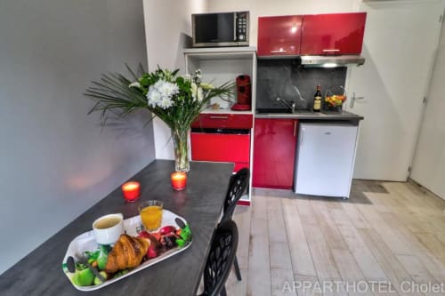 Kitchenette moderne à l'Appart'Hôtel Cholet avec petit-déjeuner, armoires rouges et table à manger