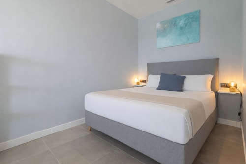 Dormitorio moderno en la casita de G&H Apartments en Jerez con cama gris, ropa blanca, arte turquesa e iluminación cálida