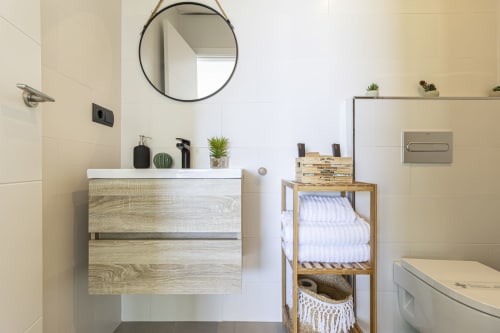 Baño moderno en la casa G&H Apartments de Jerez de la Frontera con tocador, espejo redondo y estanterías de madera