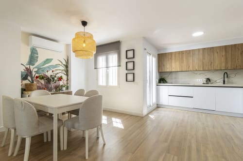 Moderna sala de estar en Apartamentos G&H Jerez con comedor, cocina, lámpara colgante amarilla y plantas en macetas