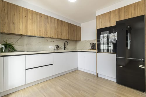 Cocina moderna en G&H Apartments Jerez con muebles blancos, gabinetes superiores de madera, salpicadero de mármol y electrodomésticos negros