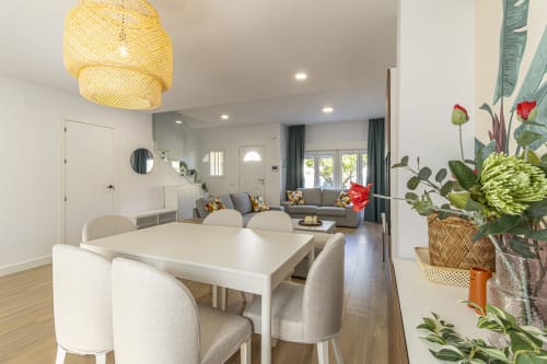 Sala moderna en G&H Apartments de Jerez con mesa de comedor, sofá gris, lámpara colgante de mimbre y flores en maceta