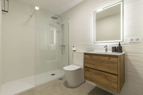 Baño moderno en G&H Apartments Jerez con ducha de paso, tocador de madera y espejo iluminado