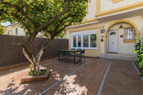 Patio con árbol maduro, mesa de comedor y entrada amarilla del apartamento en G&H Apartments, Jerez de la Frontera