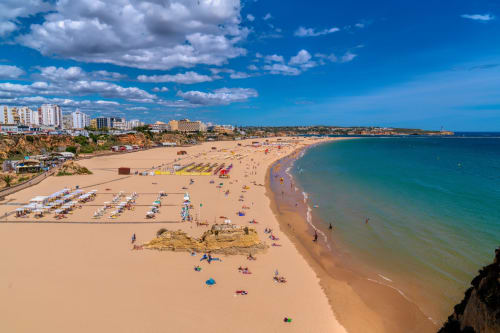 Praia de areia em Portimão com águas turquesas, banhistas e guarda-sóis coloridos sob céu azul