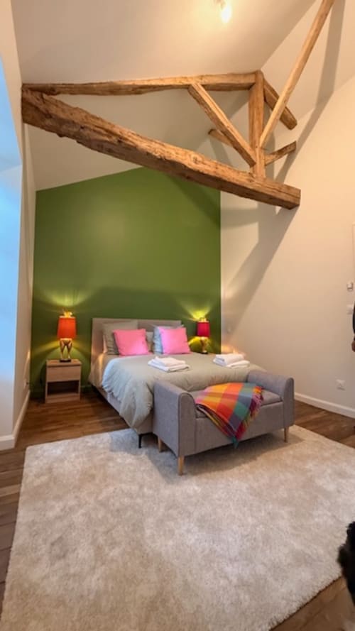 Chambre moderne aux Les Petits Nids avec mur d'accent vert, oreillers roses, poutre en bois et vue sur le jardin à Vouillé