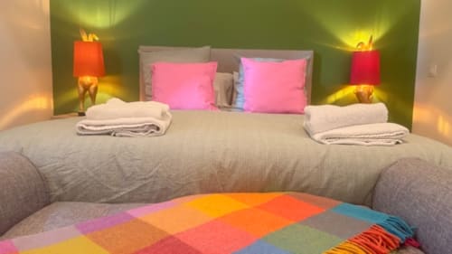 Colorful modern bedroom at Les Petits Nids with pink pillows, beige bedding, garden view, and ambient lighting in Vouillé