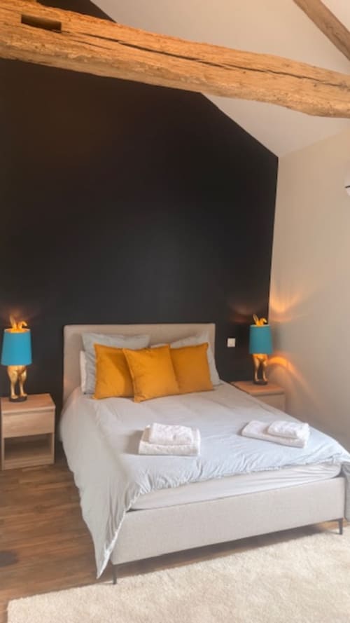 Modern bedroom at Les Petits Nids in Vouillé with white bed, gold pillows, black accent wall, wooden beam, and blue bedside