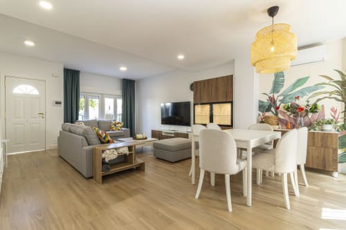 Moderna sala de estar en G&H Apartments de Jerez de la Frontera con sofá gris, mesa de comedor, TV y lámpara colgante amarilla