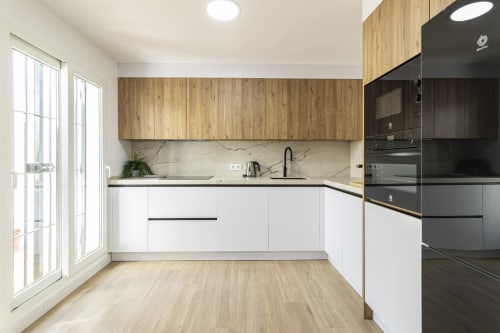 Cocina moderna en G&H Apartments Jerez con muebles blancos, detalles de madera, backsplash de mármol, electrodomésticos negros y jardín