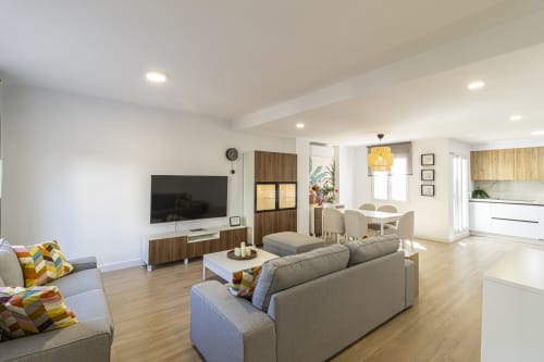Moderno salón diáfano en G&H Apartments Jerez con sofás grises, TV de pantalla plana, comedor y detalles en madera