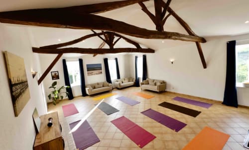 Espace de yoga du Gite La Chouette étoilée à Vaux-en-Beaujolais avec poutres en bois, tapis colorés et lumière naturelle
