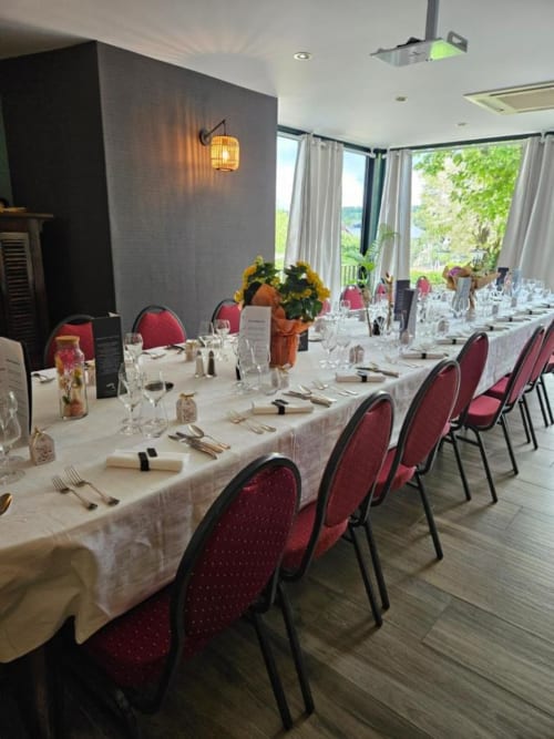 Élégante salle de banquet à La Route d'Argent, Bozouls, avec table blanche, chaises bordeaux et vue panoramique sur la vallée