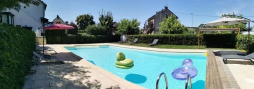 Piscine de l'Hôtel La Route d'Argent à Bozouls avec bouées colorées, transats et parasols entourés de verdure luxuriante