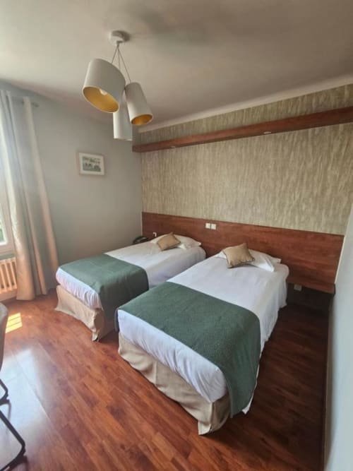Chambre twin de l'Hôtel La Route d'Argent Bozouls avec deux lits, plaids verts, tête de lit en bois et éclairage suspendu