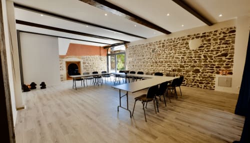 Salle de réunion moderne au Gite La Chouette étoilée à Vaux-en-Beaujolais avec murs en pierre, poutres bois et tables de conférence.