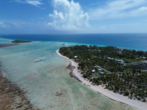 Vue aérienne du lagon turquoise de l'atoll de Tikehau, plage de sable blanc, cocotiers et bungalows dispersés à Tuherahera
