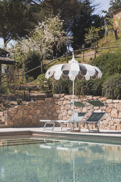 Lussuosa lounge a bordo piscina presso l'Agriturismo Il Serraglio a Montepulciano con ombrellone a righe e terrazza in pietra