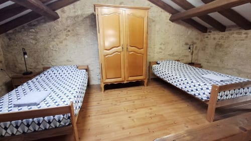 Chambre twin aux Gîtes Le Pech avec lits en bois, courtepointes bleues à motifs, armoire en bois et poutres apparentes