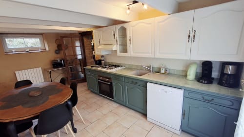 Cuisine moderne et coin repas dans la chambre La Grange aux Gîtes Le Pech à Sainte-Foy-de-Longas, avec mobilier blanc et vert.