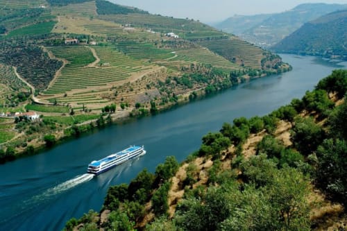 Navio de cruzeiro fluvial navegando pelo Rio Douro entre vinhedos em socalcos perto de Peso da Régua, Portugal