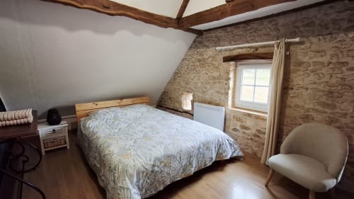 Chambre mansardée chaleureuse aux Gîtes Le Pech : poutres bois, murs en pierre, lit queen-size, fauteuil et fenêtre à Sainte-Foy-de-Longas