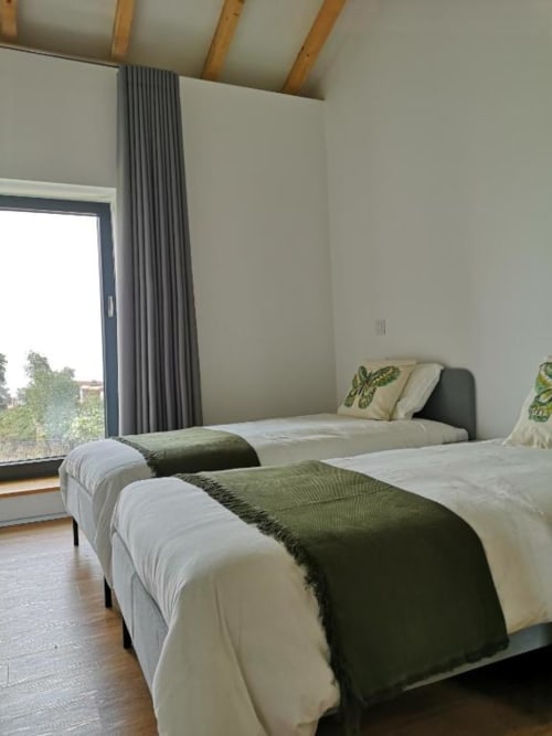 Quarto moderno com camas de solteiro, detalhes em verde, vigas de madeira e ampla janela com vista para o jardim da vila Casa da Avó Ana