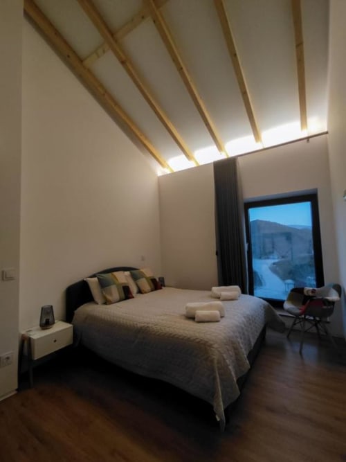 Quarto de villa moderna com teto de madeira inclinado, claraboia, cama queen, vista das montanhas por portas envidraçadas, piso de madeira