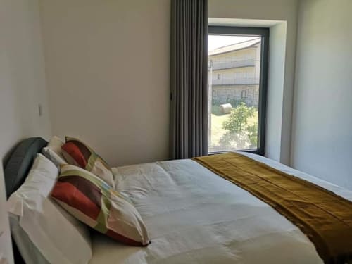 Quarto com cama, almofadas vermelhas e porta de vidro com vista para piscina e jardim da villa Casa da Avó Ana em Mondim de Basto