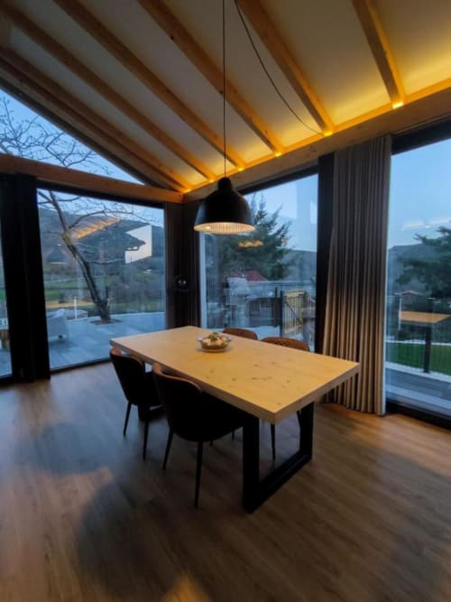 Sala de jantar moderna com mesa de madeira, cadeiras pretas e iluminação pendente com vista para a piscina e montanhas na Casa da Avó
