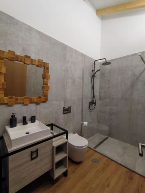 Banheiro moderno com pia branca, sanitário, chuveiro aberto, espelho com moldura de madeira e piso de madeira na villa Casa da Avó Ana