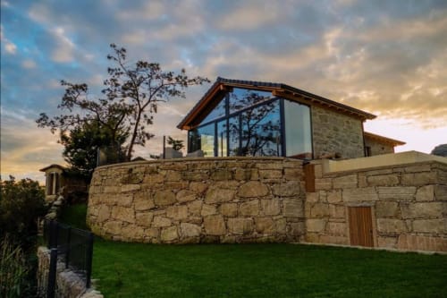 Vila de pedra com piso superior em vidro moderno na Casa da Avó Ana, Mondim de Basto, circundada por jardim verdejante e vistas de montanha