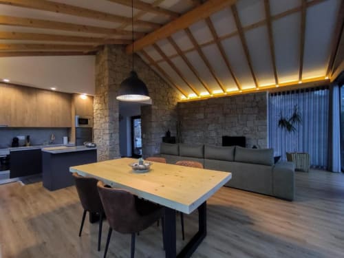 Interior de villa moderna em plano aberto com vigas de madeira, mesa de jantar, cozinha, paredes de pedra e sofá cinzento na Casa da Avó