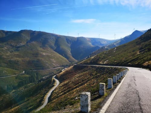 Estrada sinuosa na montanha com balizadores brancos, vista para vale verdejante e rio em Mondim de Basto, Portugal