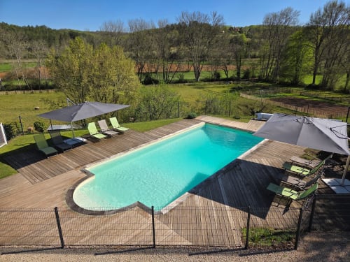 Piscine turquoise avec terrasse en bois, transats et parasols dominant la rivière et la campagne aux Gîtes Le Pech,