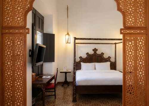 Dormitorio elegantemente amueblado en Villa Merida Boutique Hotel con puertas talladas, cama con dosel y lámparas colgantes