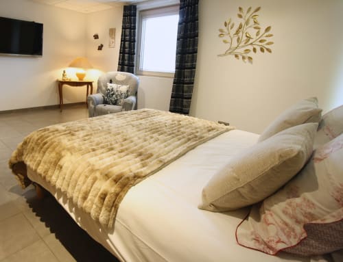 Chambre douillette de l'appartement La Gentiane au Domaine des Fleurs à Gérardmer, avec courtepointe dorée et fauteuil
