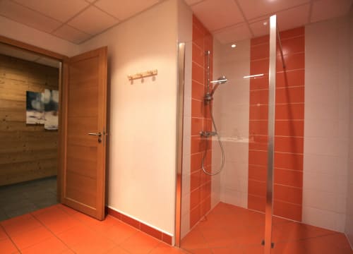 Salle de bain moderne avec douche carrelée en rouge, paroi vitrée, porte en bois au Domaine des Fleurs, Gérardmer