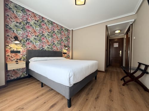 Moderna habitación del Hotel Puerto De Candás en Asturias con cama de matrimonio, pared con patrón floral y vistas a la ciudad