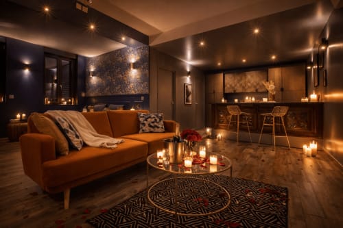 Suite spa luxueuse au Clandestin Cambrai avec canapé orange, ambiance aux chandelles et bar moderne