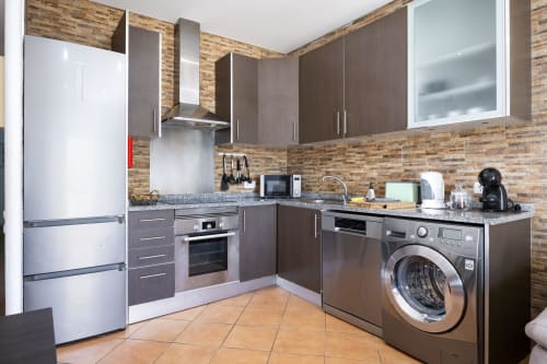 Cozinha moderna no apartamento PEDRO do hotel RB Algarve com armários escuros, eletrodomésticos em aço inoxidável e backsplash de tijolos