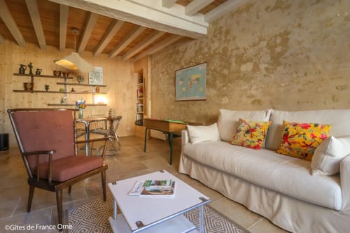 Salon rustique de la Casa Pertica B&B à Ceton, France, avec canapé crème, fauteuil bordeaux et poutres apparentes