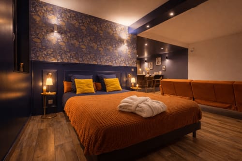 Suite luxe SPA LE CLANDESTIN Cambrai : literie orange, mur accentué sombre, éclairage ambiant et commodités spa