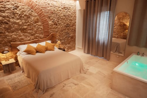Camera lussuosa con muri in pietra, biancheria crema, cuscini dorati e vasca spa turchese all'Agriturismo Il Serraglio