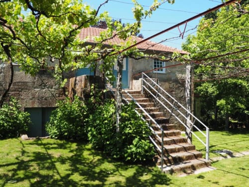 Casarão de pedra na Quinta da Coutada com jardim verdejante, escadas externas e videiras trepadeiras em Arcos de Valdevez, Portugal