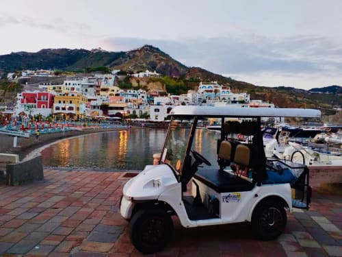 Golf car bianco parcheggiato al lungomare di Villa Bina Sea Hotel a Serrara Fontana, tra edifici colorati e barche