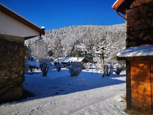 Vallée de montagne enneigée avec chalets traditionnels, pics forestiers et beau jour d'hiver aux Gîtes les Grandes voies
