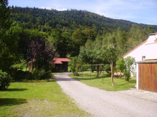 Allée en gravier menant au Chalet Cossu aux Gîtes les Grandes voies, entouré de pelouses verdoyantes, d'arbres et de montagnes boisées
